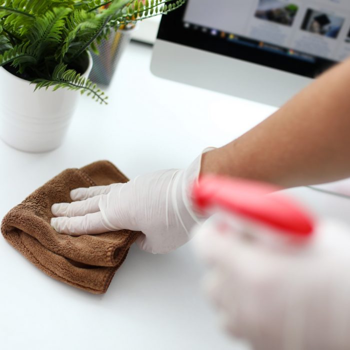Precisely clean office table Focus on gloved male hand holding doormat and swiping dust inhabited by harmful bacteria from white workplace with concentration and diligence. Pleasant clean-up concept. Blurred background